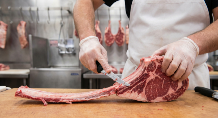 Butcher frenching a tomahawk steak rib bone, scraping meat clean from the bone