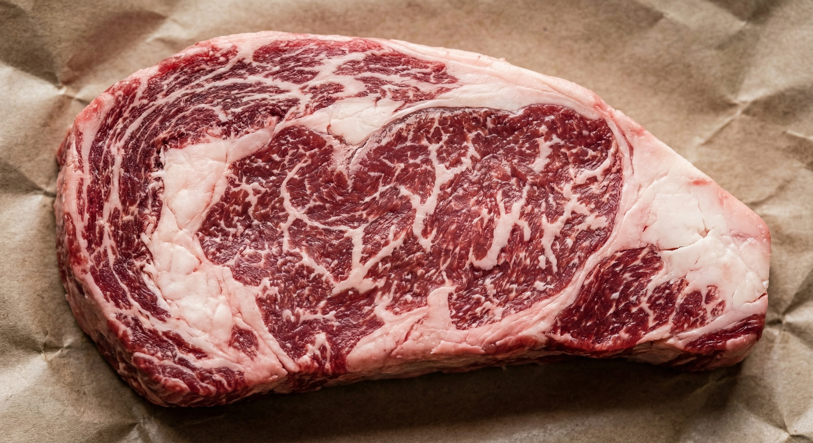 Close-up of a raw ribeye steak showing abundant white intramuscular marbling throughout the red meat